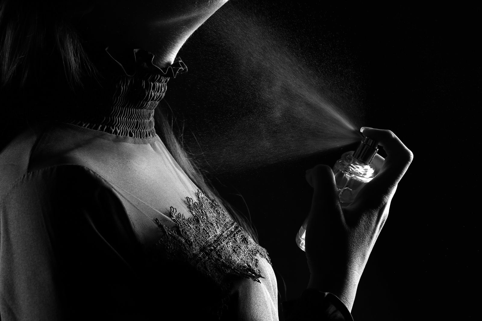Black-and-white studio portrait of a woman spraying perfume